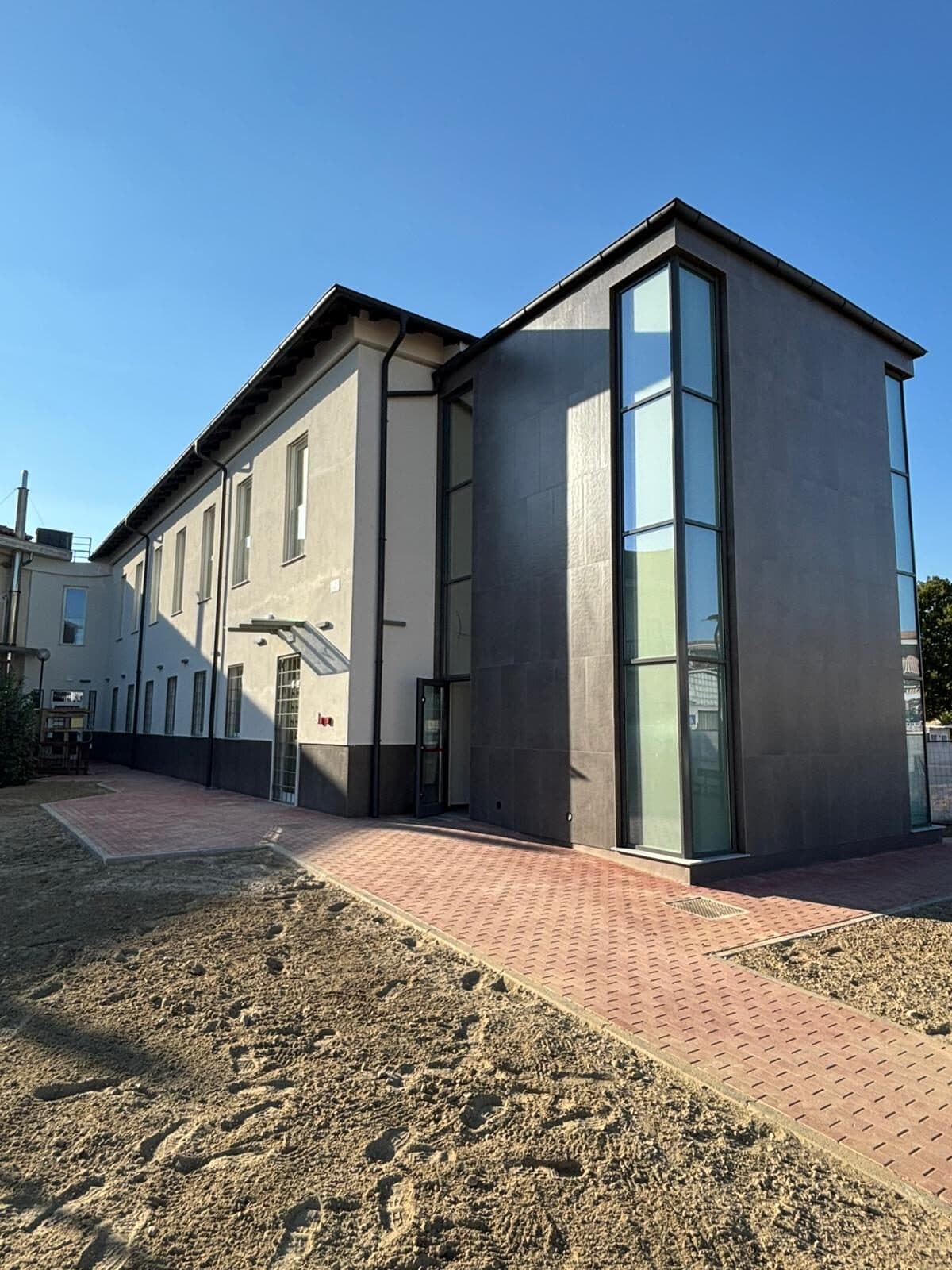 Edificio a due piani con un volume rivestito in lastre scure e lunghe vetrate verticali in alluminio