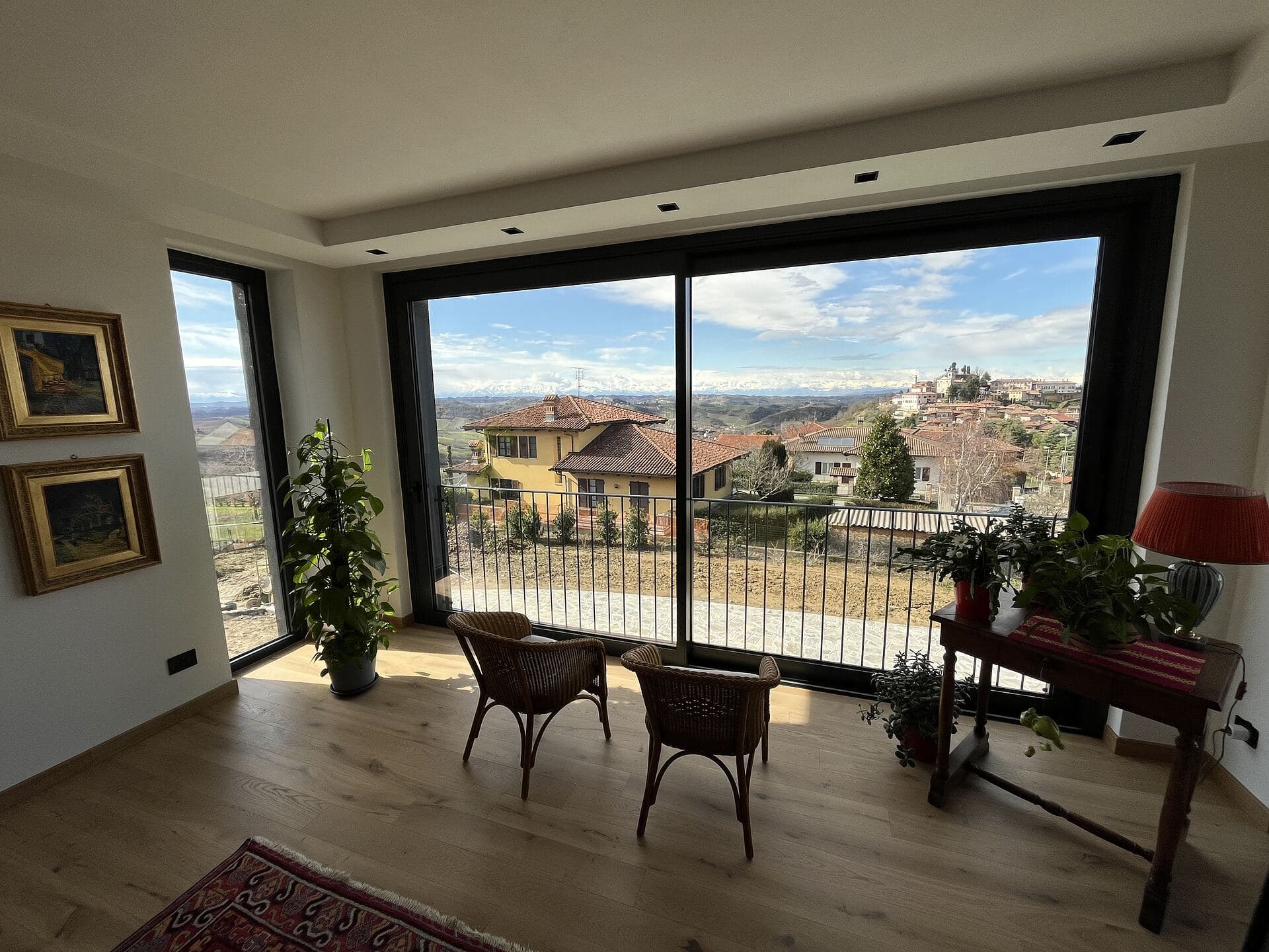 Il salone con lo scorrevole d'angolo aperto sulla valle, il paese in collina oltre il vetro e il terrazzo davanti