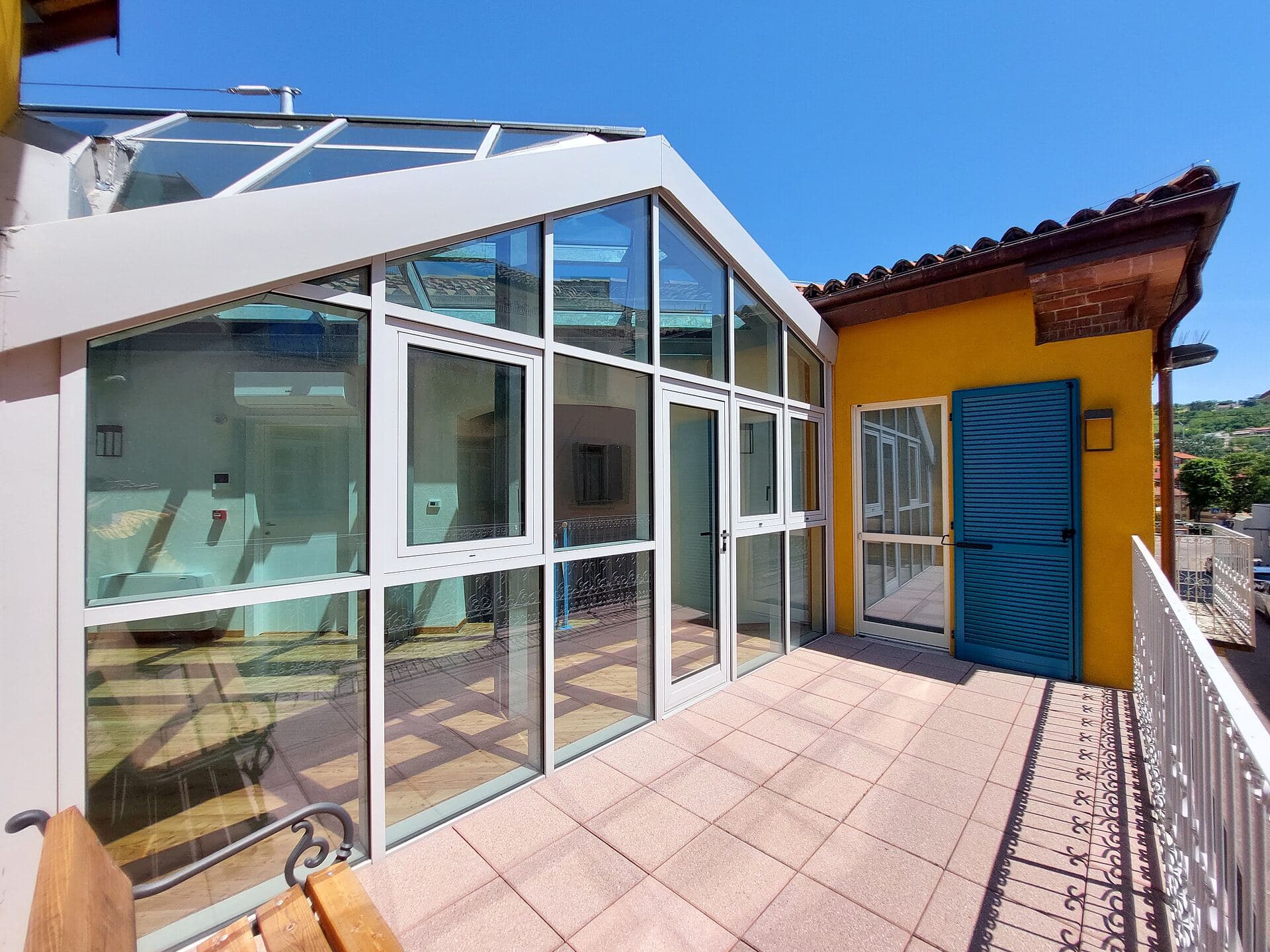 La veranda vista dal terrazzo, con la copertura in vetro a falde e la porta azzurra della corte accanto